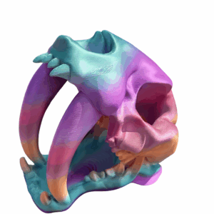 3D-printed Sabertooth Dice Tower made from shimmering tri-color silk filament with shades of aqua, violet, and gold, shaped like a sabertooth skull.